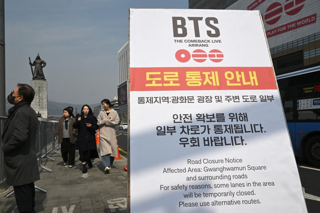 Photo by JUNG YEON-JE / AFP. This picture taken on March 16, 2026 shows pedestrians passing a road closure notice for a comeback concert of K-pop boy group BTS at Gwanghwamun Square in Seoul.