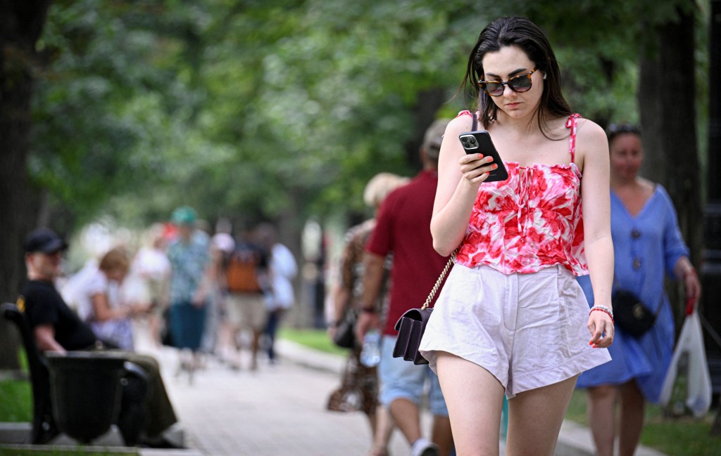 A pedestrian woman uses her smart phone in Moscow on July 30, 2025. Russia has drastically restricted press freedom and freedom of speech online, with a new legislation that will slap fines on internet users who search for web pages, books, artwork or music albums that the authorities deem "extremist"; a term that has a very broad definition in Russia that can refer to terrorist groups and political opponents alike. (Photo by Alexander NEMENOV / AFP)