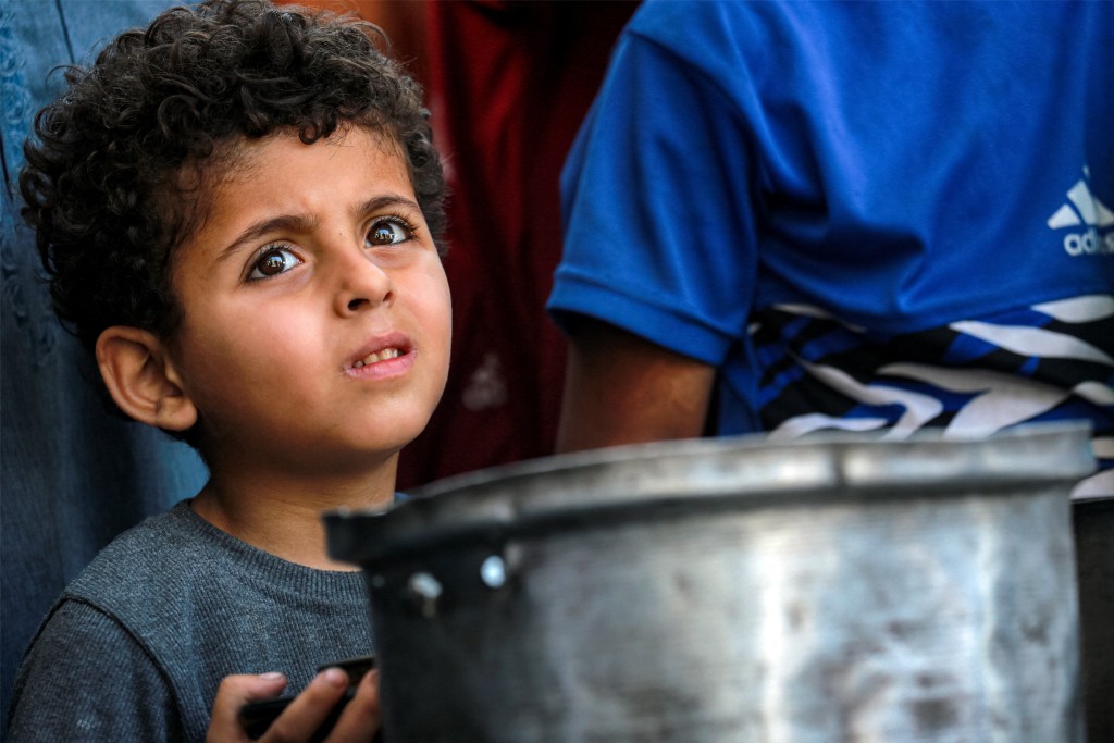 A boy looks on as he stands between people queueing with pots to receive meals from a charity kitchen in Gaza City on July 14, 2025. (Photo by Bashar TALEB / AFP)