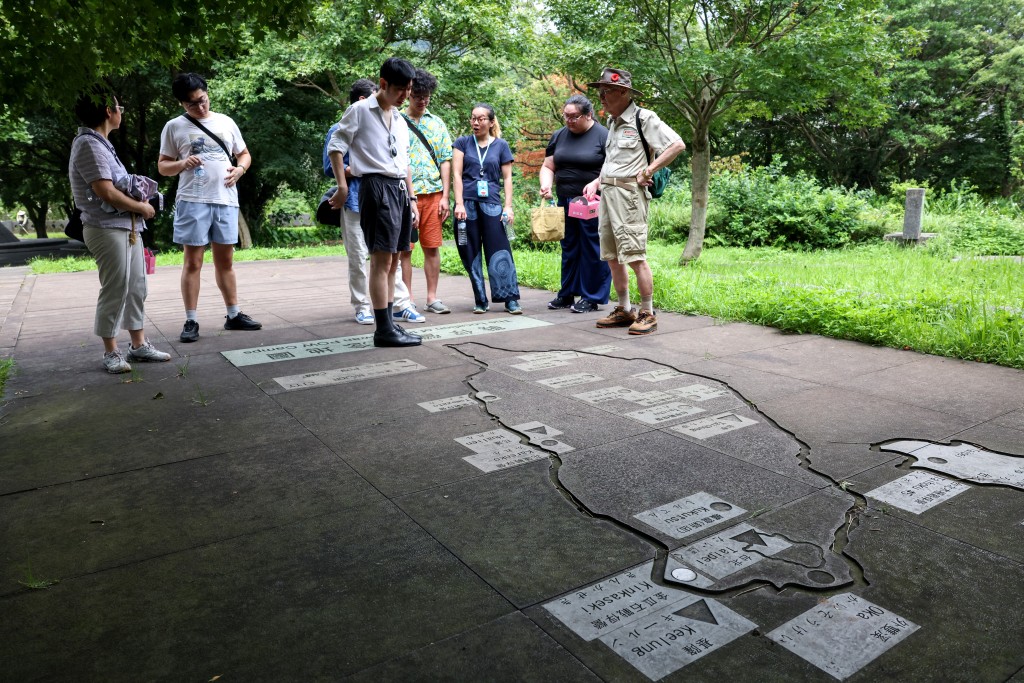 Michael Hurst (R), founder and director of the Taiwan Prisoners of War (POW) Camps Memorial Society, leads a tour and introduces a map of POW camps around Taiwan at Taiwan POW Memorial and Peace Park, in New Taipei City on July 31, 2025 In a small urban park in Taiwan, more than 4,000 names are etched into a granite wall -- most of them British and American servicemen held by the Japanese during World War II. (Photo by I-Hwa Cheng / AFP)