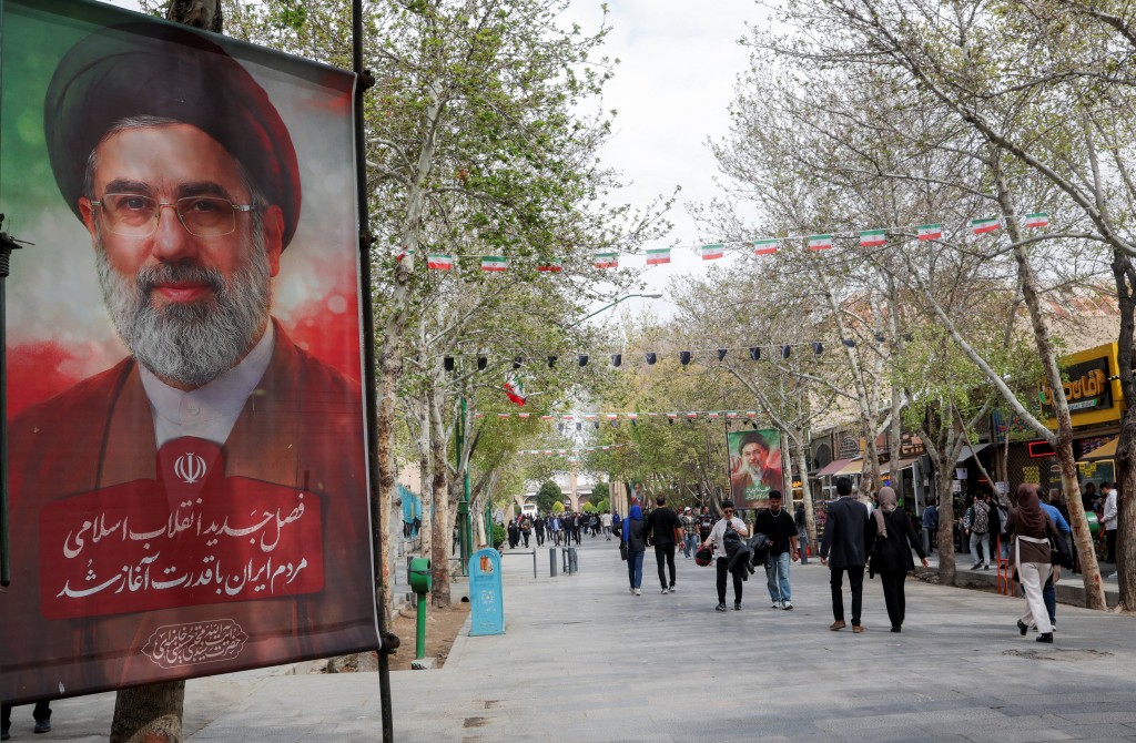 People walk past posters of Iran's new Supreme Leader, Mojtaba Khamenei, displayed along a street in Isfahan, Iran, March 24, 2026. REUTERS/Alaa Al Marjani