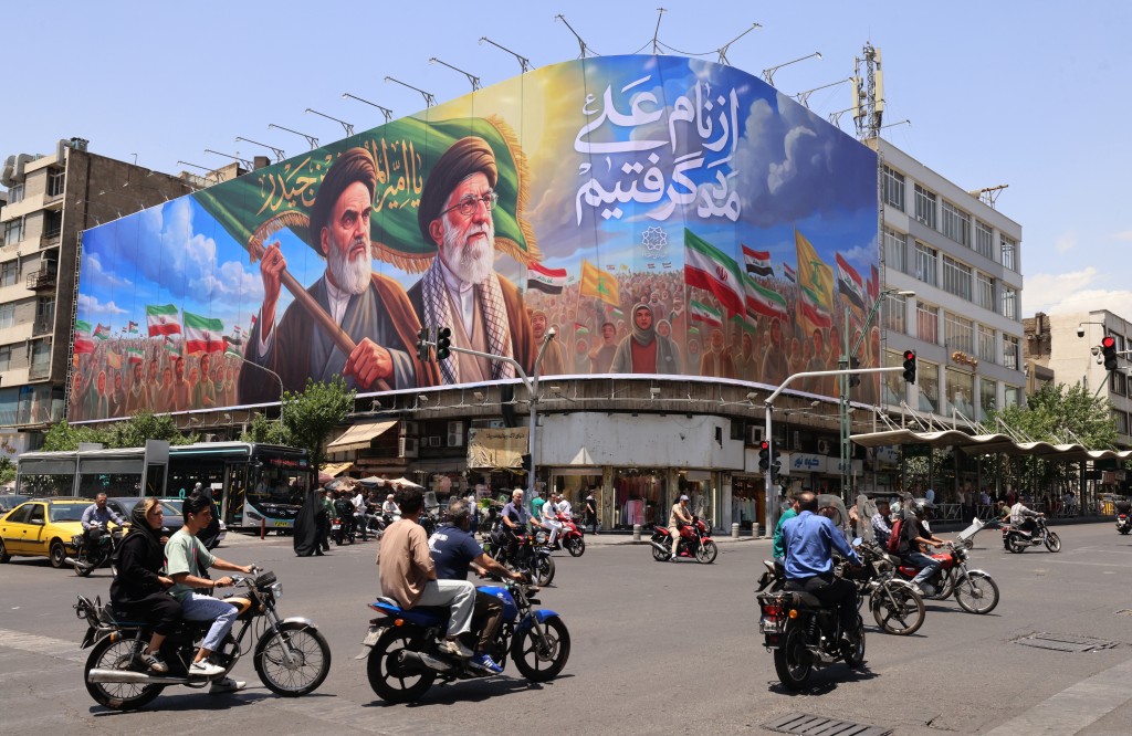 Photo by ATTA KENARE / AFP  People ride motorcycles past a large billboard showing portraits of Iran's late supreme leader, Ayatollah Ruhollah Khomeini (L) and slain supreme leader Ayatollah Ali Khamenei (R) in central Tehran on June 8, 2026.
