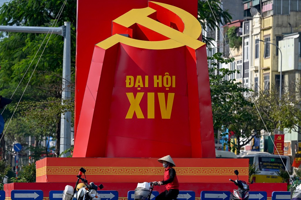 Photo by NHAC NGUYEN / AFP  A woman rides a bicycle past a billboard advertising the 14th Congress of the Vietnamese Communist Party in Hanoi on January 8, 2026.