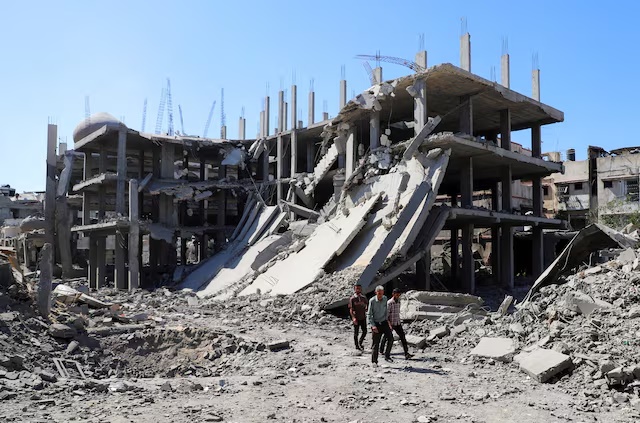 Palestinians walk past a destroyed building, as they inspect the damage in the aftermath of Israeli operation at Sabra neighbourhood in Gaza City, October 8, 2025. REUTERS/Ebrahim Hajjaj