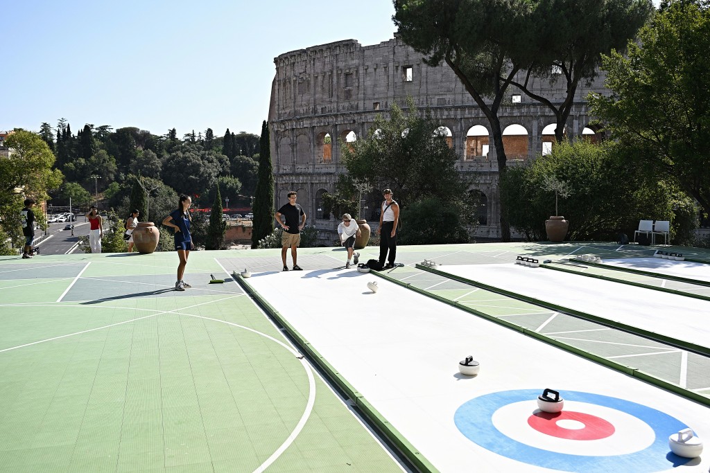 TOPSHOT - People try the winter sport of curling on ice-free synthetic curling rinks set up in Colle Oppio Park overlooking the Colosseum during a hot summer day in Rome on August 24, 2026. (Photo by Andreas SOLARO / AFP)