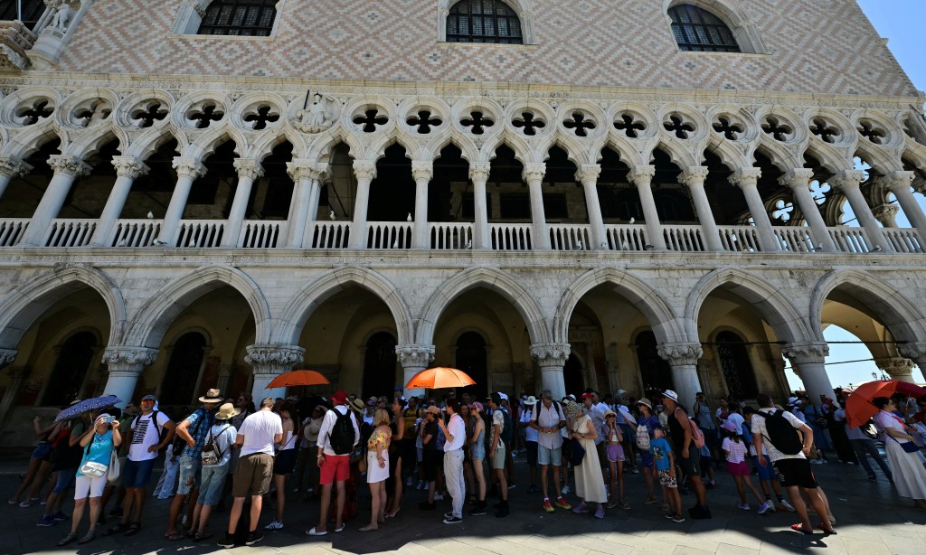 Tourists stand in the shade while visiting in St. Mark's Square during a heatwave in Venice on June 27, 2026. (Photo by Stefano RELLANDINI / AFP)