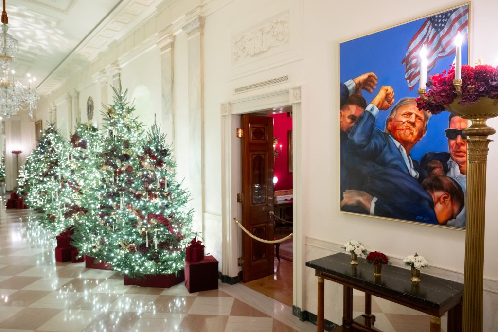 A painting of US President Donald Trump depicting the assassination attempt in Pennsylvania hangs in the Cross Hall as it is decorated with Christmas decorations at the White House in Washington, DC, December 1, 2025, during a Christmas decoration media tour. (Photo by SAUL LOEB / AFP)