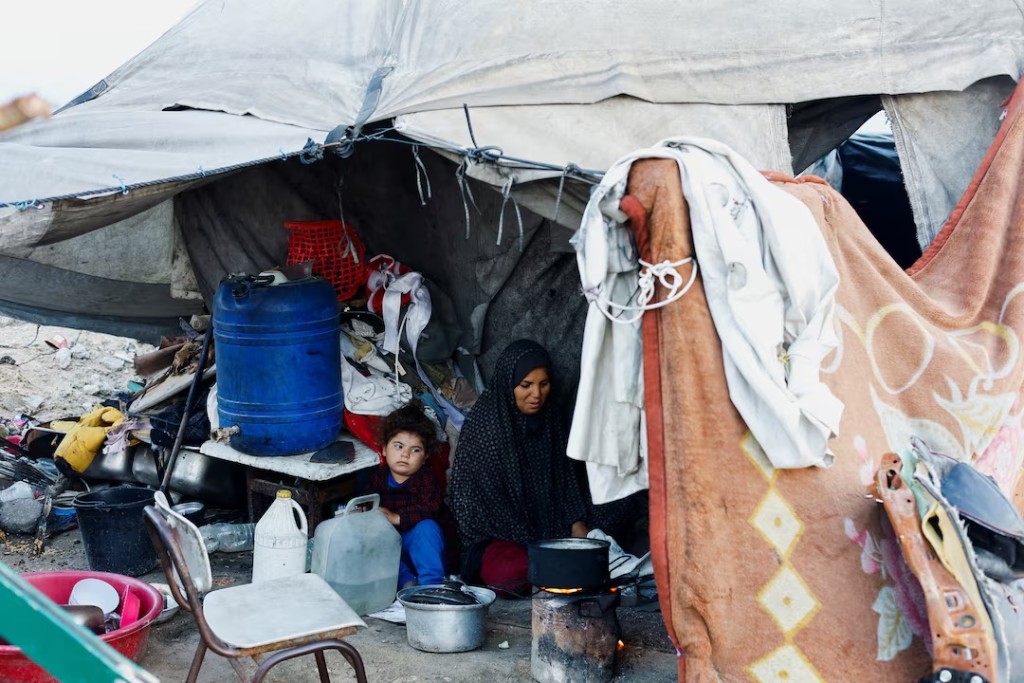 A Palestinian family prepares food over a fire stove in front of their tent in a camp on a rainy day in Nuseirat, central Gaza Strip, November 25, 2025. REUTERS/Mahmoud Issa 