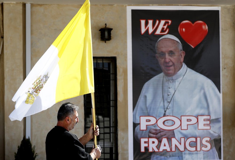 A Christian priest holds a Vatican flag as he walks by a poster of Pope Francis during preparations for the Pope's visit in Mar Youssif Church in Baghdad, Iraq, Friday, February 26, 2021. A Christian priest holds a Vatican flag as he walks by a poster of Pope Francis during preparations for the Pope's visit in Mar Youssif Church in Baghdad, Iraq, Friday, February 26, 2021.