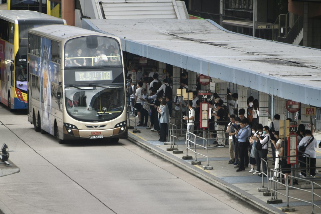 A crowd of students wearing masks waits in line at a bus stop under a heavy rainstorm, with a double-decker bus arriving amidst the flooding caused by Cyclone Wipha in Hong Kong.