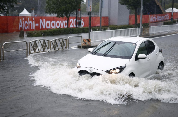 A car drives along a road flooded by heavy rain while banners for the Aichi-Nagoya Asian Games are visible in the background in Nagoya. REUTERS