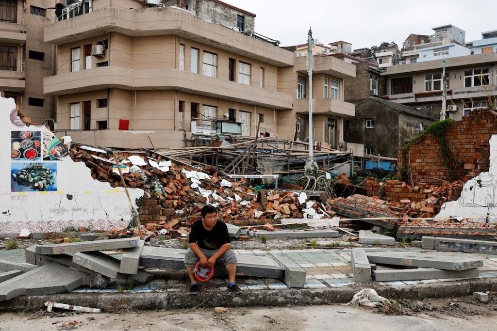A person sits beside a collapsed wall in the aftermath of Typhoon Bavi in the coastal village of Dongsha, Taizhou, Zhejiang province, China, July 12, 2026. REUTERS/Go Nakamura
