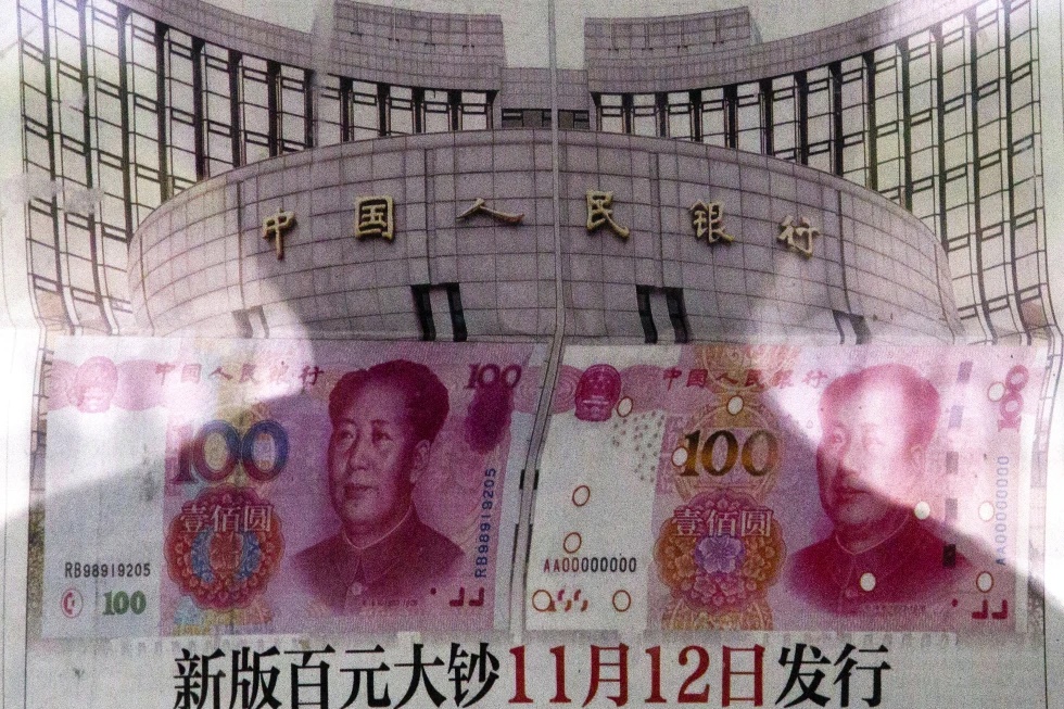 In this Aug. 11, 2015 photo, a shadow of a man is reflected on a glass as he reads a newspaper reporting China’s central bank or People’s Bank of China announced the 2015 edition of the 100 renminbi notes will be issued starting from November 12, at a stand in Beijing. (AP Photo/Andy Wong, File)
