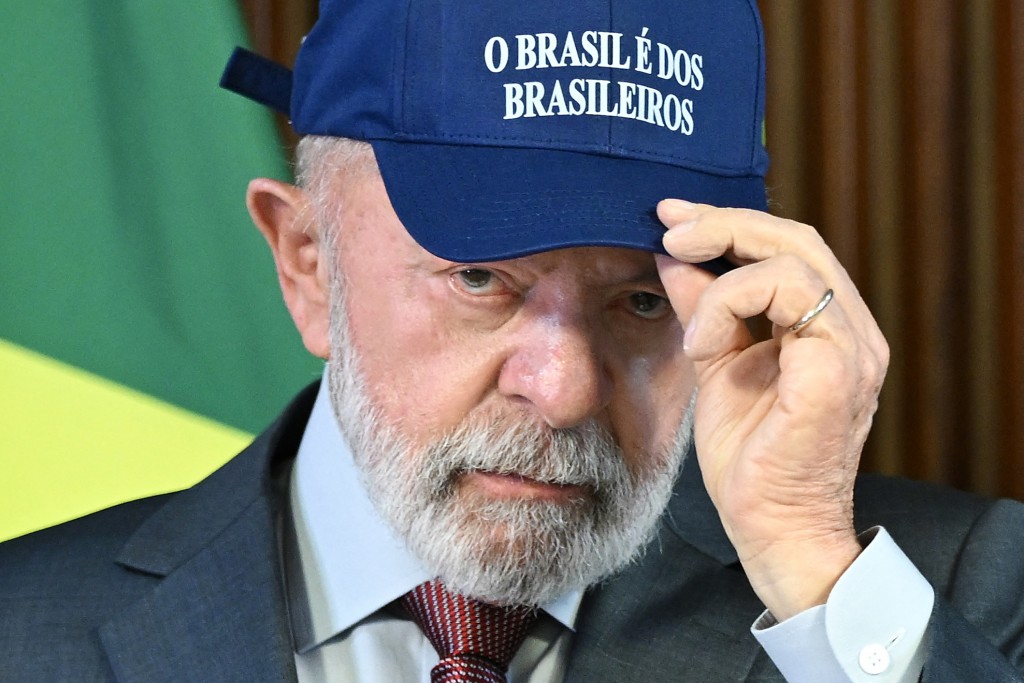 Photo by EVARISTO SA / AFP. Brazil's President Luiz Inacio Lula da Silva puts on a cap reading "Brazil belongs to Brazilians" during a ministerial meeting at the Planalto Palace in Brasilia on August 26, 2025.