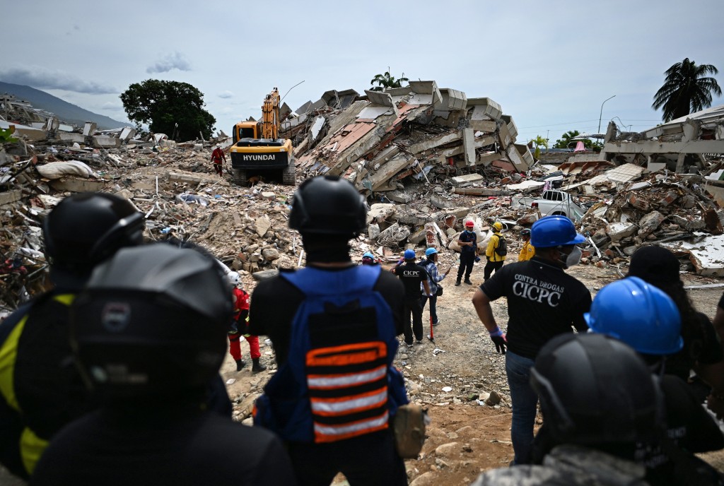 Photo by JUAN BARRETO / AFP  Volunteers and paramedics stand still as rescuers carry out sound tests in search of survivors following the June 24 twin earthquakes, in Caraballeda, La Guaira state, Venezuela, on June 30, 2026.