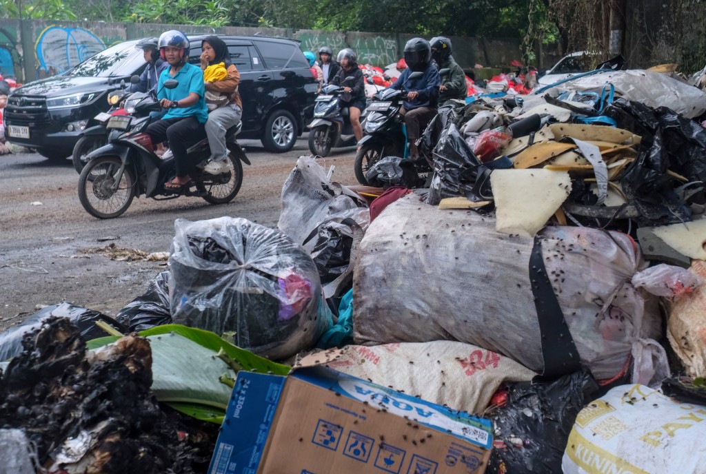 Photo by BAY ISMOYO / AFP. This picture taken on January 20, 2026, shows vehicles driving along a road littered with illegally dumped waste by residents in Pamulang, South Tangerang, Banten.