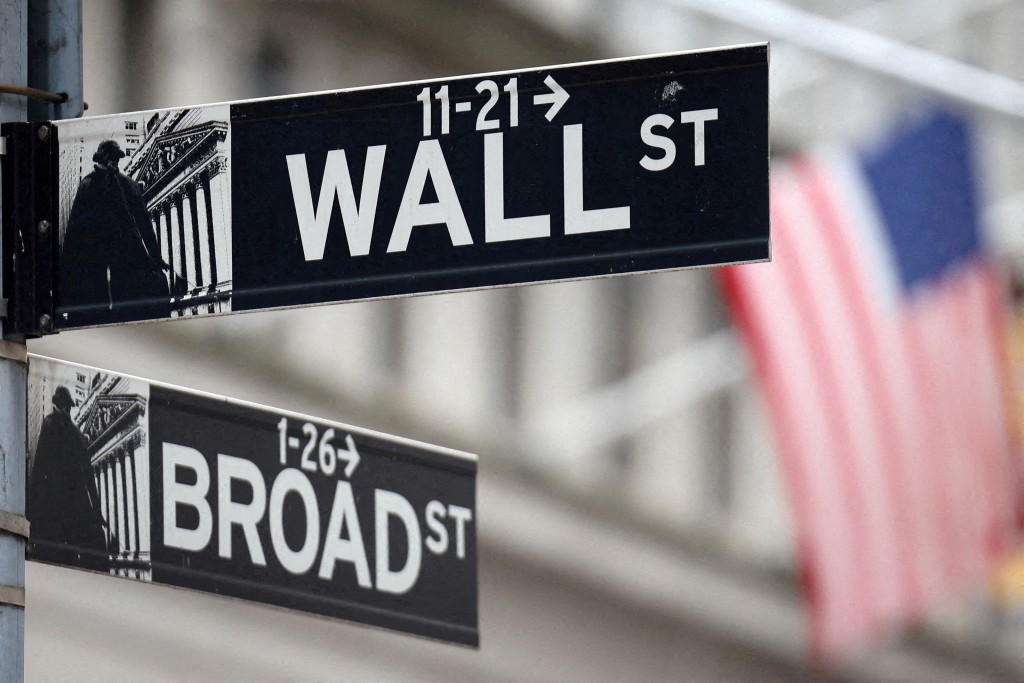 A Wall Street sign hangs in front of a U.S. Flag outside the New York Stock Exchange (NYSE) before the Federal Reserve announcement in New York City, U.S., September 18, 2024. REUTERS/Andrew Kelly/File Photo