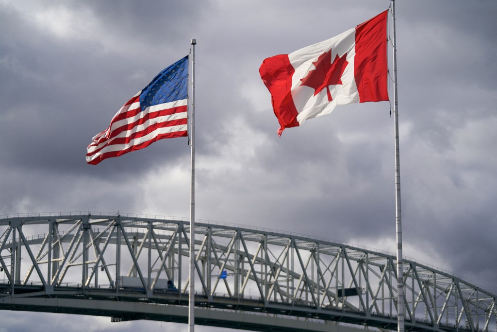 Photo by GEOFF ROBINS / AFP. The US and Canada flags flutter next to the Blue Water Bridge border crossing in Point Edward, Ontario, on October 24, 2025.