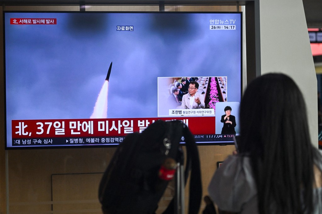 Photo by PEDRO PARDO / AFP  A woman watches a television screen showing a news broadcast with file footage of a North Korean missile test, at a train station in Seoul on May 26, 2026.