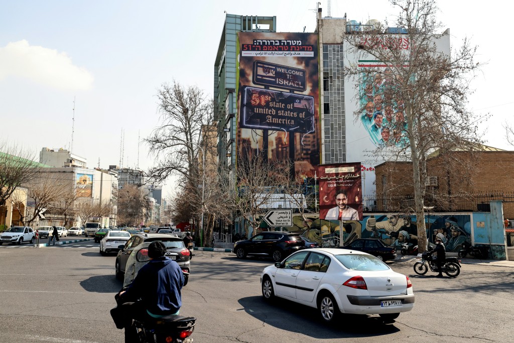 Vehicles drive past an anti-Israeli and anti-US billboard hanging from a building that reads in Persian "The target is clear: Trump's 51st state" on Palestine Square in Tehran on February 25, 2026. (AFP)