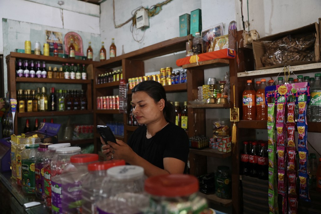Photo by NIHARIKA KULKARNI / AFP  This photograph taken on August 31, 2026 shows restaurant and bar owner Pushpa Karki using a mobile phone at her restaurant along the Punatsangchhu River in Bhutan's Wangdue Phodrang district.