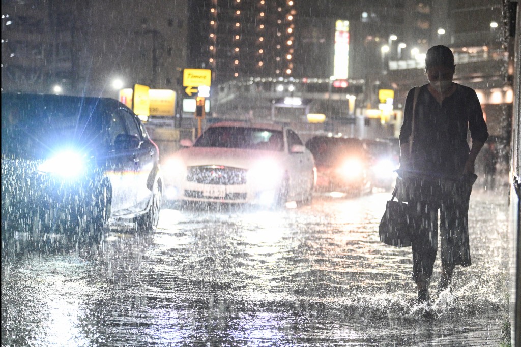 Cars pass a commuter on a flooded road near Chiba metro station in Chiba. (AFP)