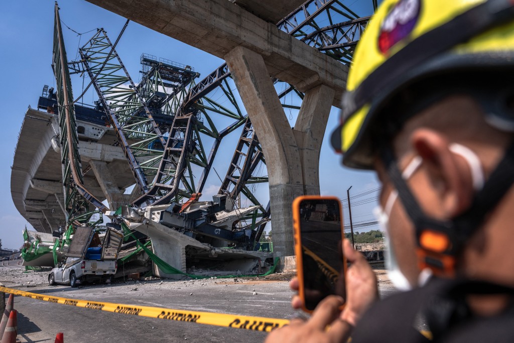 Photo by CHANAKARN LAOSARAKHAM / AFP  A recovery worker takes pictures at the site of a construction crane collapse onto a highway in Samut Sakhon on the outskirts of Bangkok on January 15, 2026.