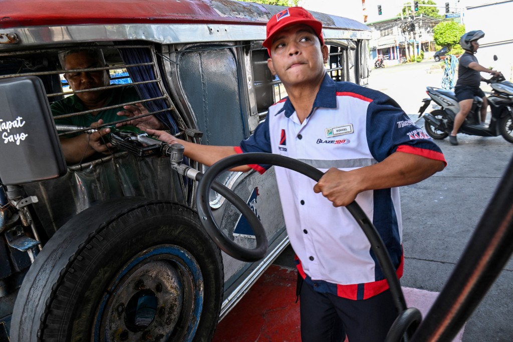 Photo by TED ALJIBE / AFP  Jeepney driver Eric Helera (L) refuels his vehicle with diesel at a fuel station in Manila on March 23, 2026.