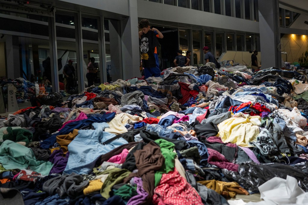 Photo by MANAURE QUINTERO / AFP  A boy tries a t-shirt from a pile of clothes at a refugee camp at a baseball stadium in La Guaira, on June 26, 2026.