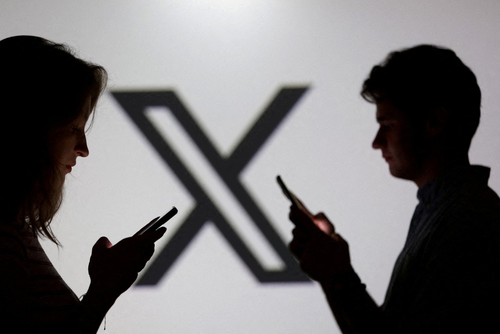 Teenagers pose for a photo while holding smartphones in front of a X logo in this illustration taken September 11, 2025. REUTERS/Dado Ruvic/Illustration/File Photo