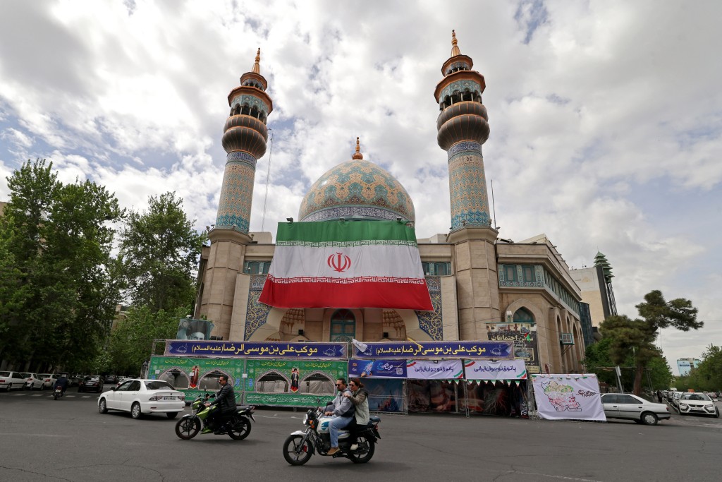 Motorists ride past the Imam Sadiq (AS) mosque with a giant Iranian flag installed on its front at the Palestine Square in Tehran on April 19, 2026. (AFP)