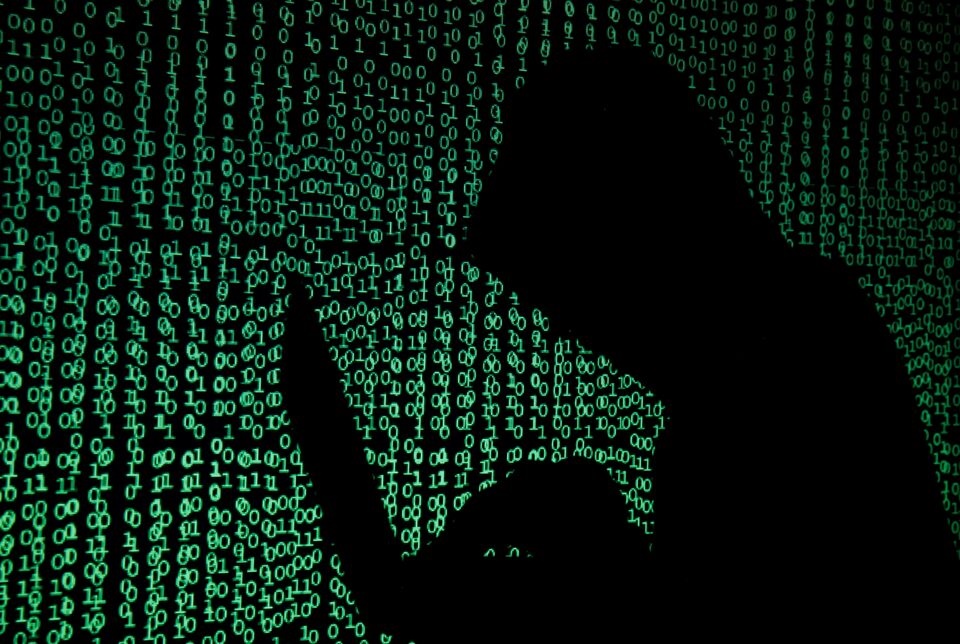 A hooded man holds a laptop computer as cyber code is projected on him in this illustration picture taken on May 13, 2017. REUTERS/Kacper Pempel/Illustration/File Photo