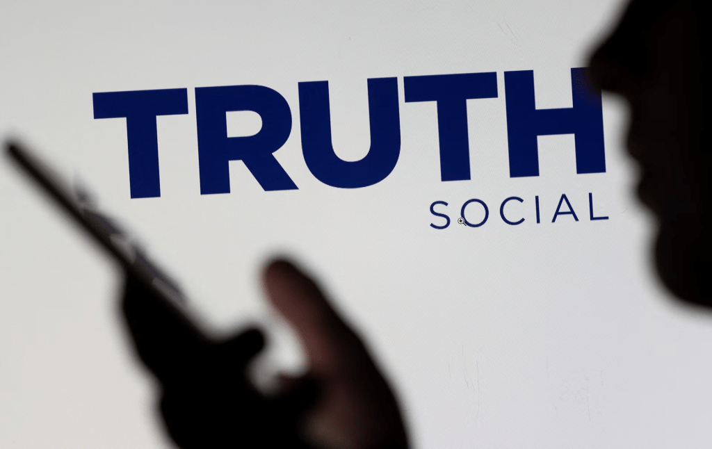 The Truth social network logo is seen displayed behind a woman holding a smartphone in this picture illustration taken February 21, 2022. REUTERS/Dado Ruvic/Illustration/File Photo