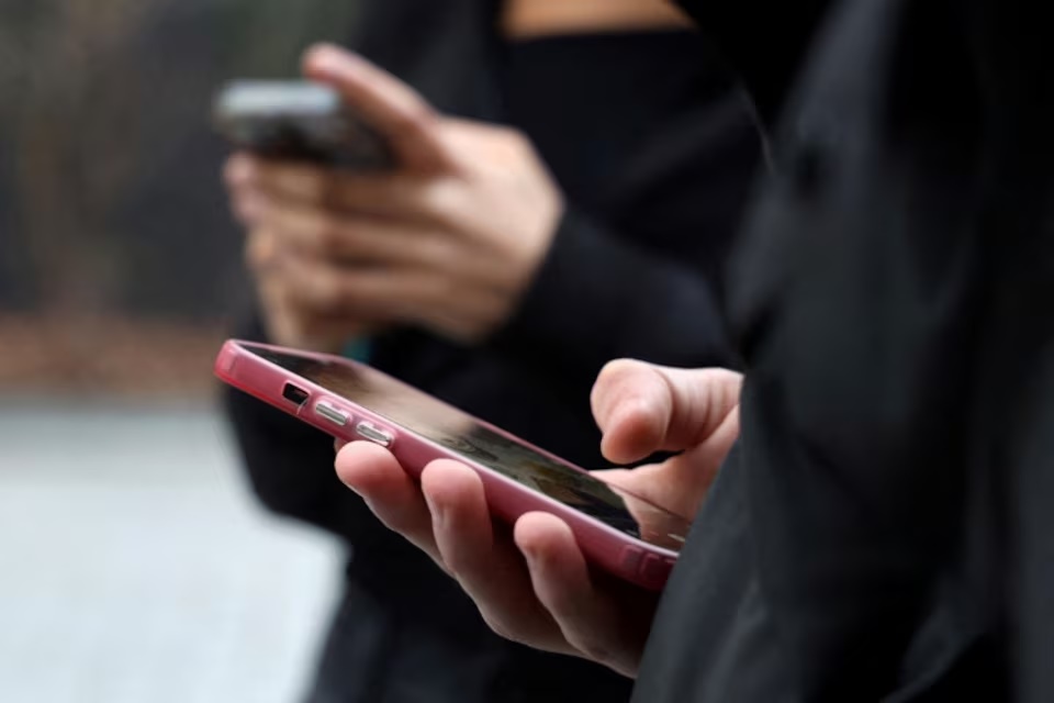 Teenagers look at their mobile phone screens during an interview with Reuters about the bill aimed at banning the use of social networks for those under 15 and mobile phones in high schools from the start of the 2026 school year, in Paris, France, February 20, 2026. REUTERS/Manuel Ausloos/File Photo