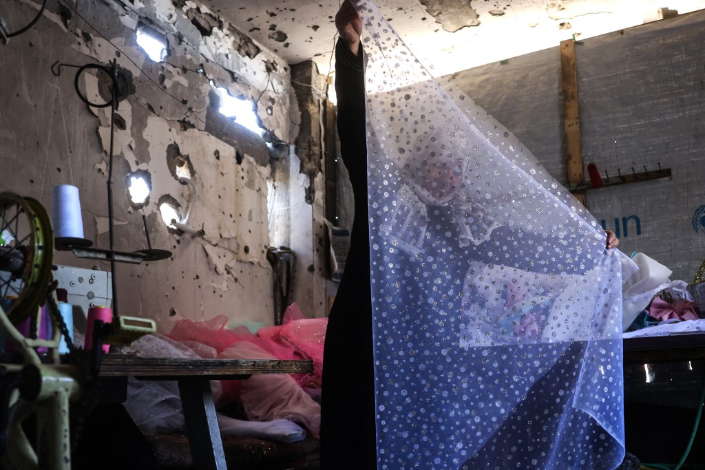 Photo by BASHAR TALEB / AFP A Palestinian dressmaker folds the cloth for a gown, at a workshop where dresses are created including evening and wedding gowns despite limited resources and old dresses are recycled, in the city of Khan Yunis in the southern Gaza Strip on June 13, 2026.