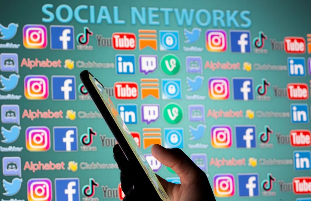 Woman with smartphone is seen in front of displayed social media logos in this illustration taken, May 25, 2021. REUTERS/Dado Ruvic/Illustration/File Photo 