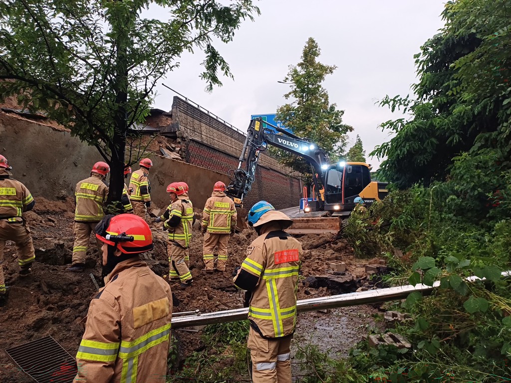 Rescue members searching for missing people after a 10-metre-high (33-foot) retaining wall from an overpass collapsed onto the road during a heavy rain in Osan. (AFP)