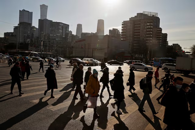 People cross a street during morning rush hour in front of the skyline of the central business district (CBD) in Beijing, China December 15, 2020. REUTERS/Thomas Peter 