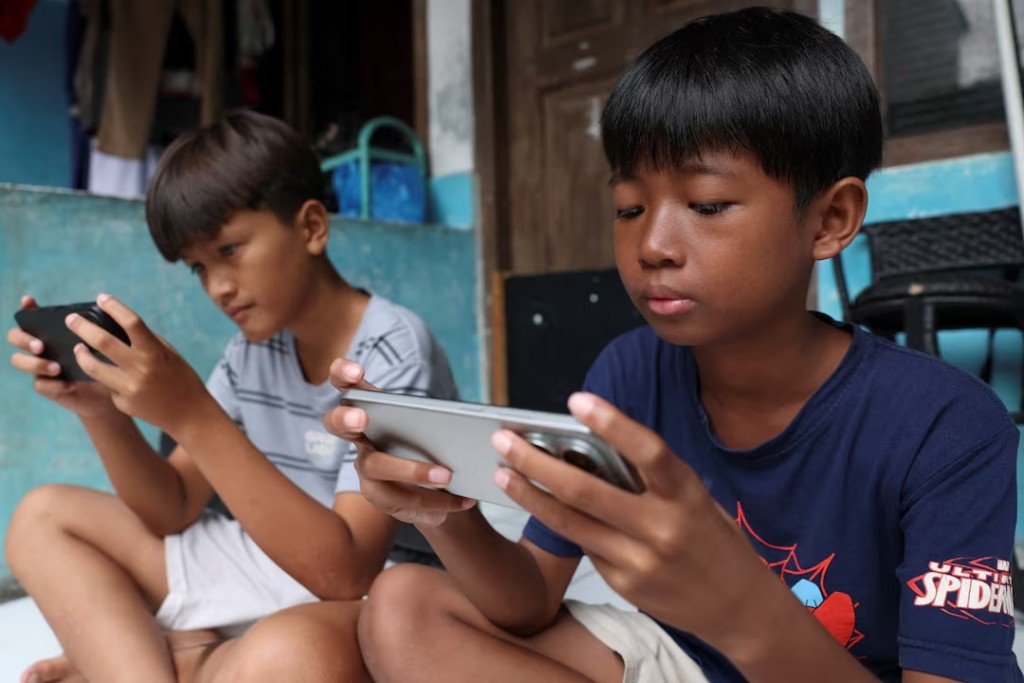 Affan Haritsah, 11 and Kevin Prince, 14, play games on their phones, as Indonesia's communications and digital information ministry implements restrictions against "high-risk" social media platforms, including Facebook, TikTok, and Roblox, in Depok, on the outskirts of Jakarta, Indonesia, March 28, 2026. REUTERS/Ajeng Dinar Ulfiana