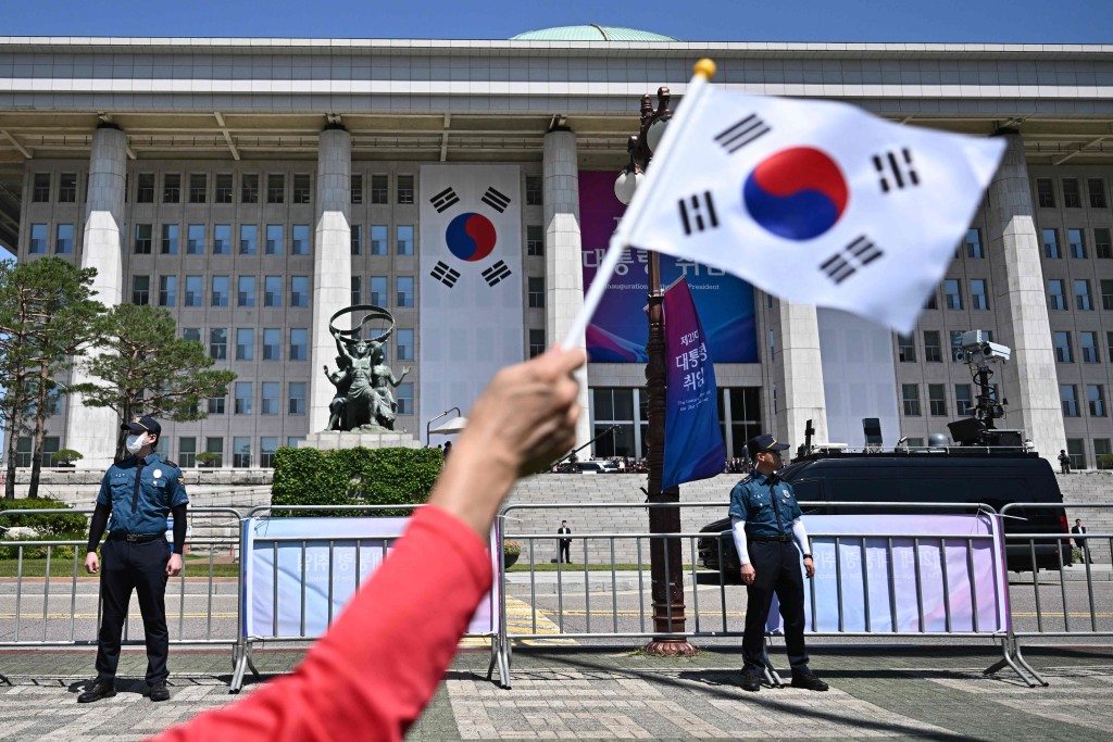 A person waves a flag of South Korea as police stand guard outside the National Assembly ahead of the inauguration of South Korea's President Lee Jae-myung in Seoul on June 4, 2025. AFP