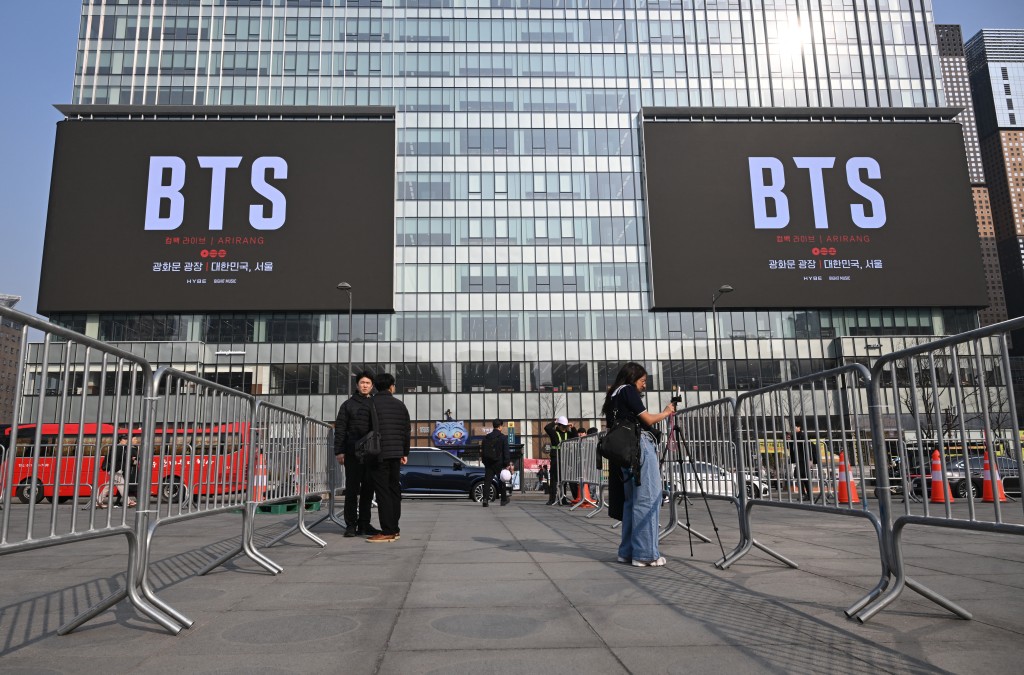 Photo by JUNG YEON-JE / AFP  People stand in front of billboards promoting a comeback concert of K-pop boy group BTS at Gwanghwamun Square in Seoul on March 17, 2026.