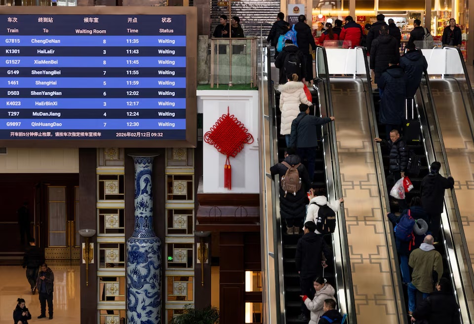 People stand on an escalator next to a screen displaying train information at Beijing Railway Station during annual Spring Festival travel rush, in Beijing, China, February 12, 2026. REUTERS/Maxim Shemetov