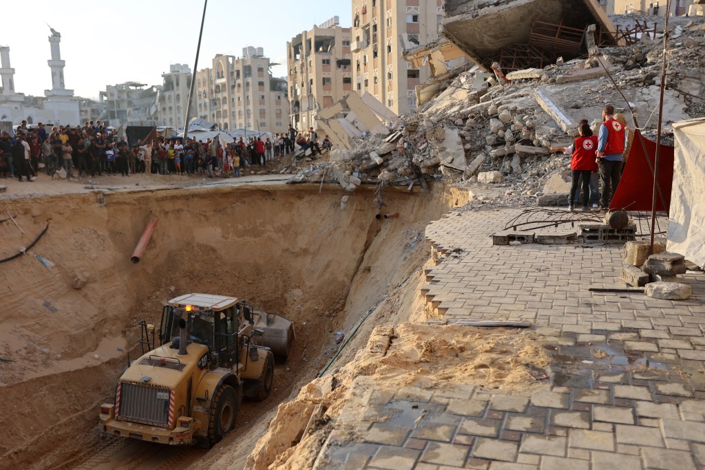 People and members of the International Committee of the Red Cross (ICRC) watch, as Palestinians use an excavator to dig deep into the ground, reportedly searching for bodies in Khan Yunis in the southern Gaza Strip on October 17, 2025.  Photo by OMAR AL-QATTAA / AFP