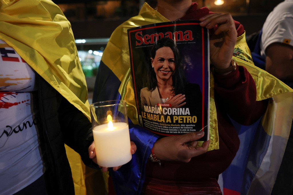 People hold a candle and a magazine with an image of Nobel Peace Prize winner Maria Corina Machado, as Venezuelans living in Colombia gather for a global march in support of Machado in Bogota, Colombia, December 6, 2025. REUTERS/Luisa Gonzalez