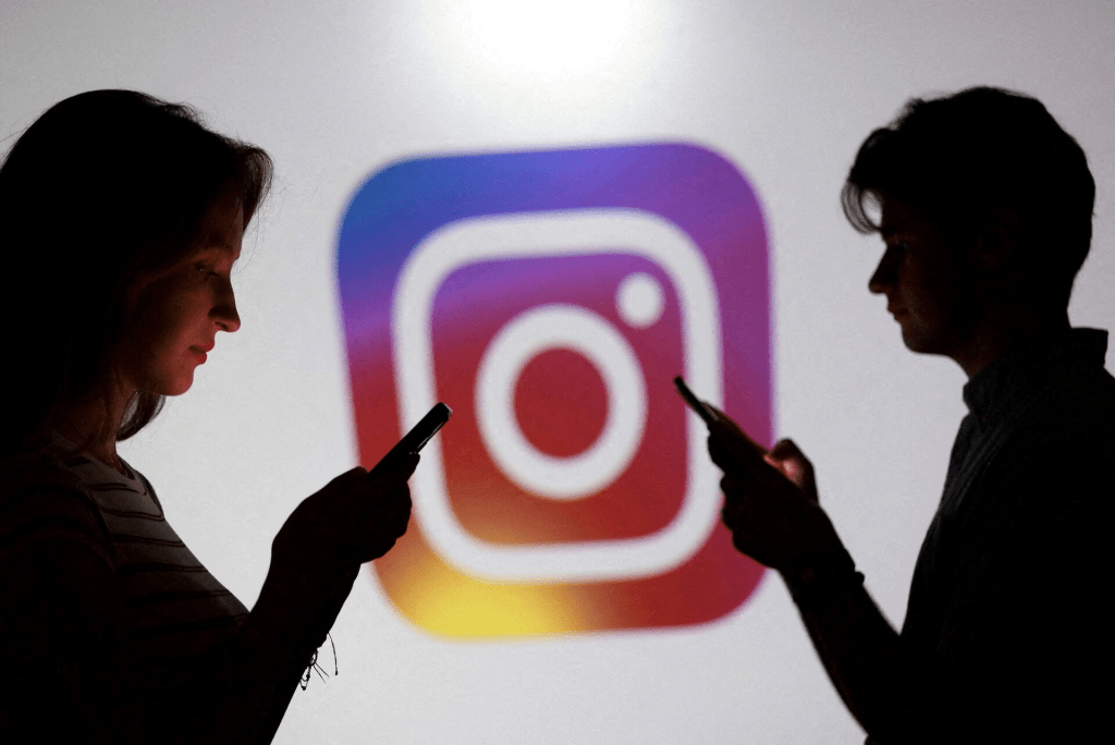 Teenagers pose for a photo while holding smartphones in front of an Instagram logo in this illustration created on September 11, 2025. REUTERS/Dado Ruvic/Illustration/File Photo