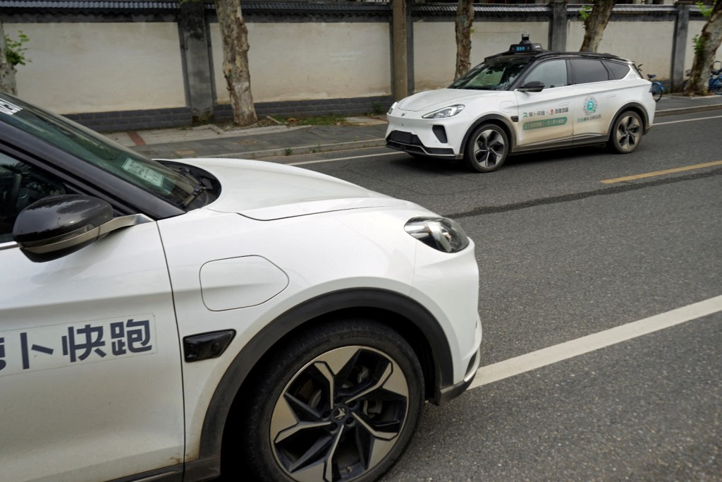 A driverless car by Apollo Go, Baidu's robotaxi service, drives past another Apollo Go robotaxi parked on the side of a road in Wuhan, Hubei province in July 2024. Photo by REUTERS