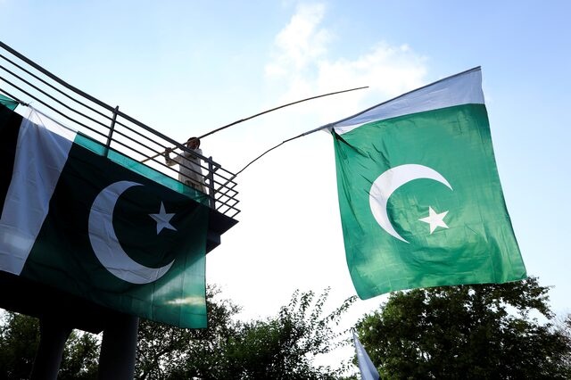 A boy uses a bamboo stick to adjust national flags at an overhead bridge ahead of Pakistan's Independence Day, in Islamabad, Pakistan August 10, 2018. REUTERS/Faisal Mahmood 
