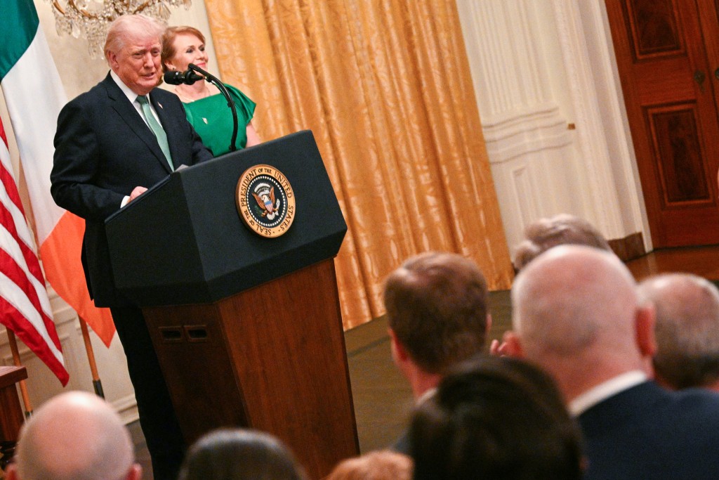 US President Donald Trump speaks Irish Prime Minster Micheal Martin's wife Mary O'Shea looks on, on the occasion of St. Patrick's Day, in the East Room of the White House in Washington, DC, on March 17, 2026. (Photo by Jim WATSON / AFP)