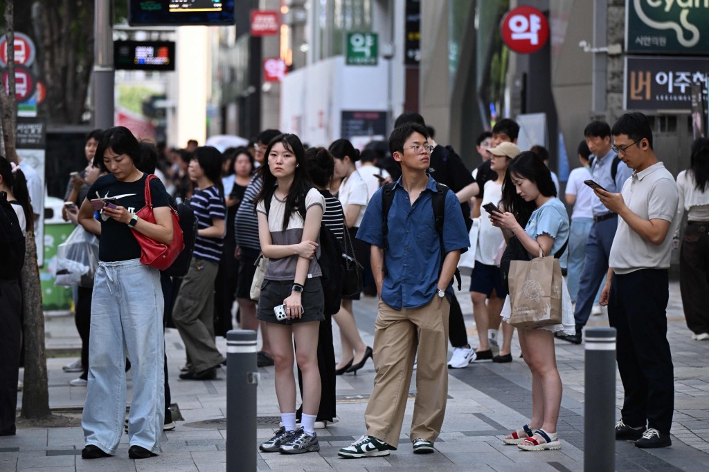 People wait for a bus on a hot day in Seoul on August 7, 2026. (Photo by Greg Baker / AFP)