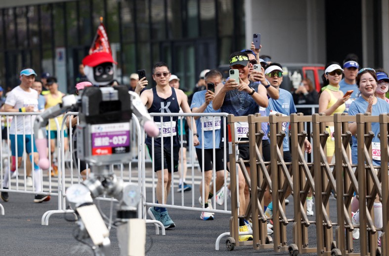 Human runners take out their smartphones to take photos of a humanoid robot. REUTERS